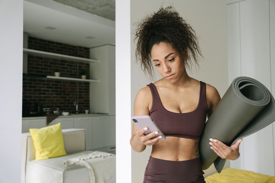 A woman with a yoga mat checking her smartphone at home, preparing for a workout.