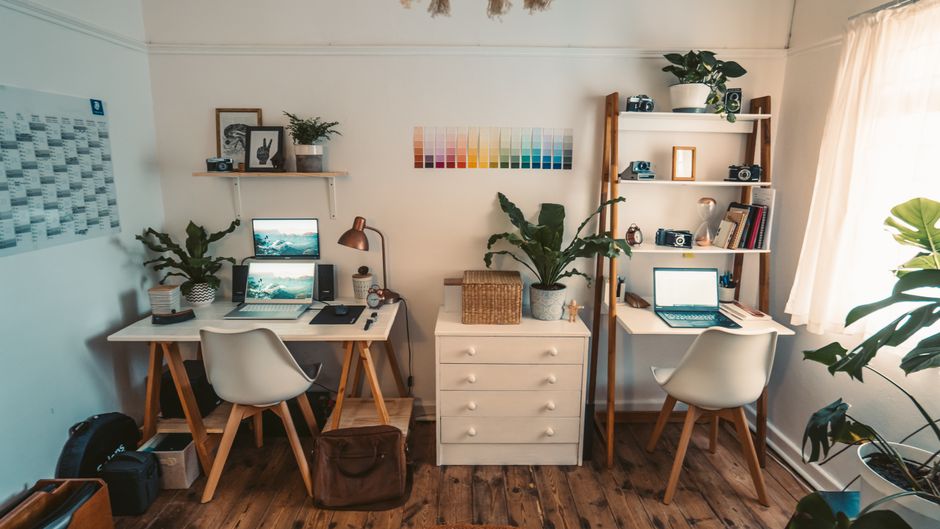 A well-organized home office featuring dual desks, laptops, indoor plants, and natural light.